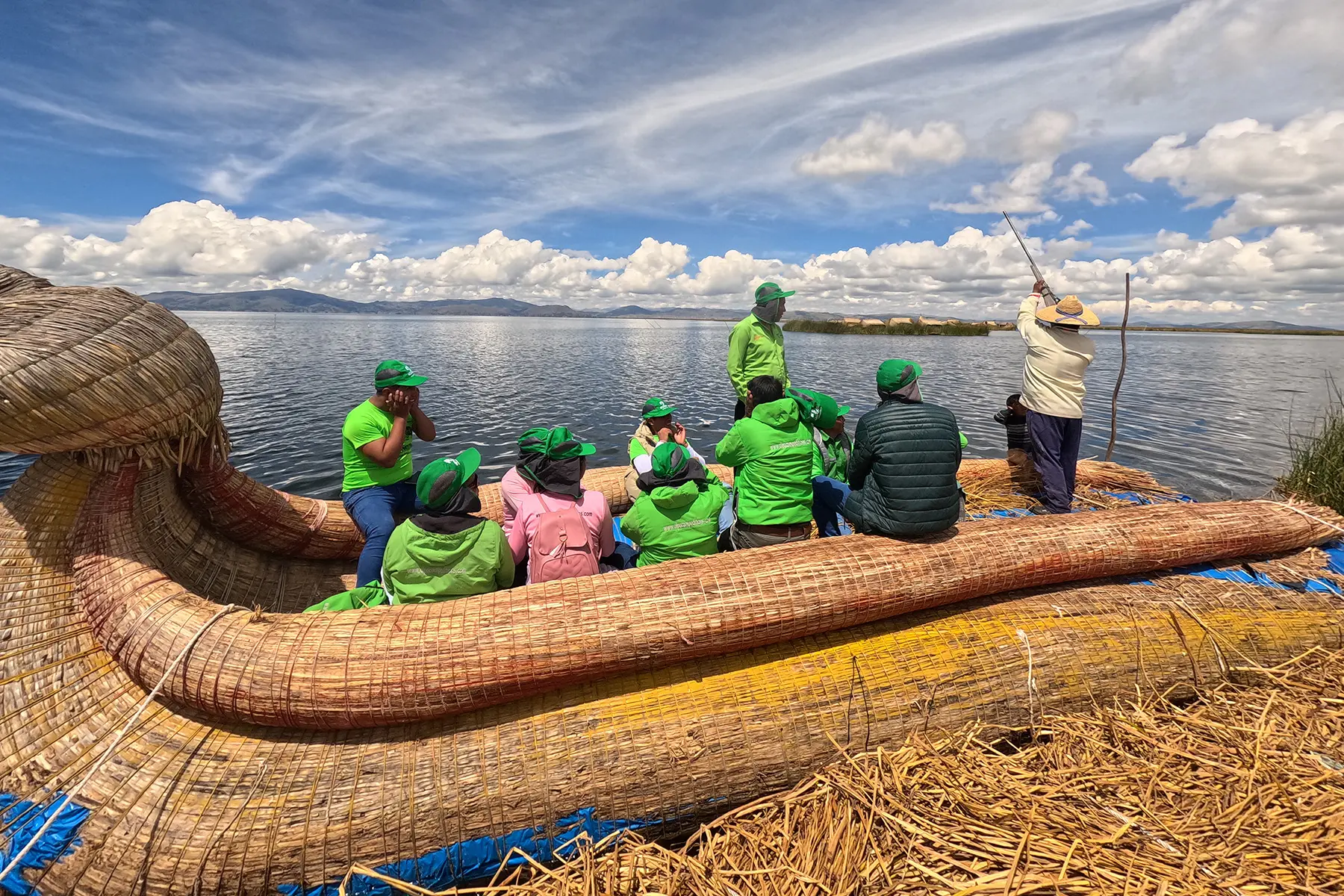Alpaca Expeditions porters sitting on totora reeds while visiting the floating islands of Lake Titicaca.